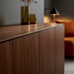 ### Key Elements

- **Main Subjects**: Wooden cabinet, decorative vases, lamp, and armchair.
- **Objects**: Two glass vases, one with dried flowers, and a table lamp.
- **Notable Features**: Rich wood grain of the cabinet, warm color palette, and soft lighting.
- **Text or Symbols**: None present.

### Overall Mood or Theme
The image conveys a warm, inviting atmosphere with a focus on modern, minimalist design. The combination of natural materials and soft lighting creates a cozy and stylish interior space.